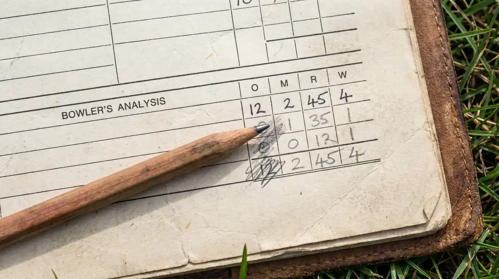 Cricket scorer working out bowler economy rate in pencil in a paper scorebook with calculations visible