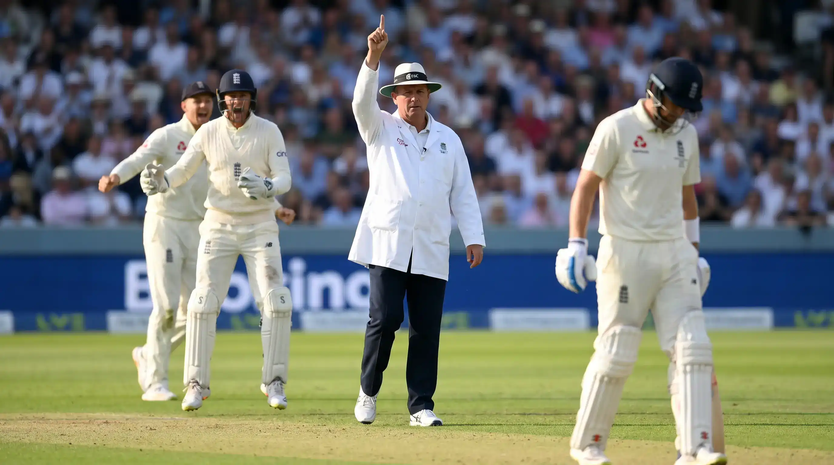 On-field cricket umpire raising the index finger to give a batter out caught behind after a successful edge review