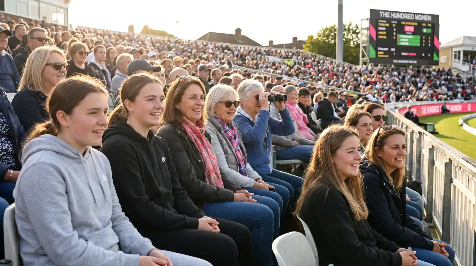 Group of female cricket fans of varied ages watching a Hundred women's match together in the stands of an English ground