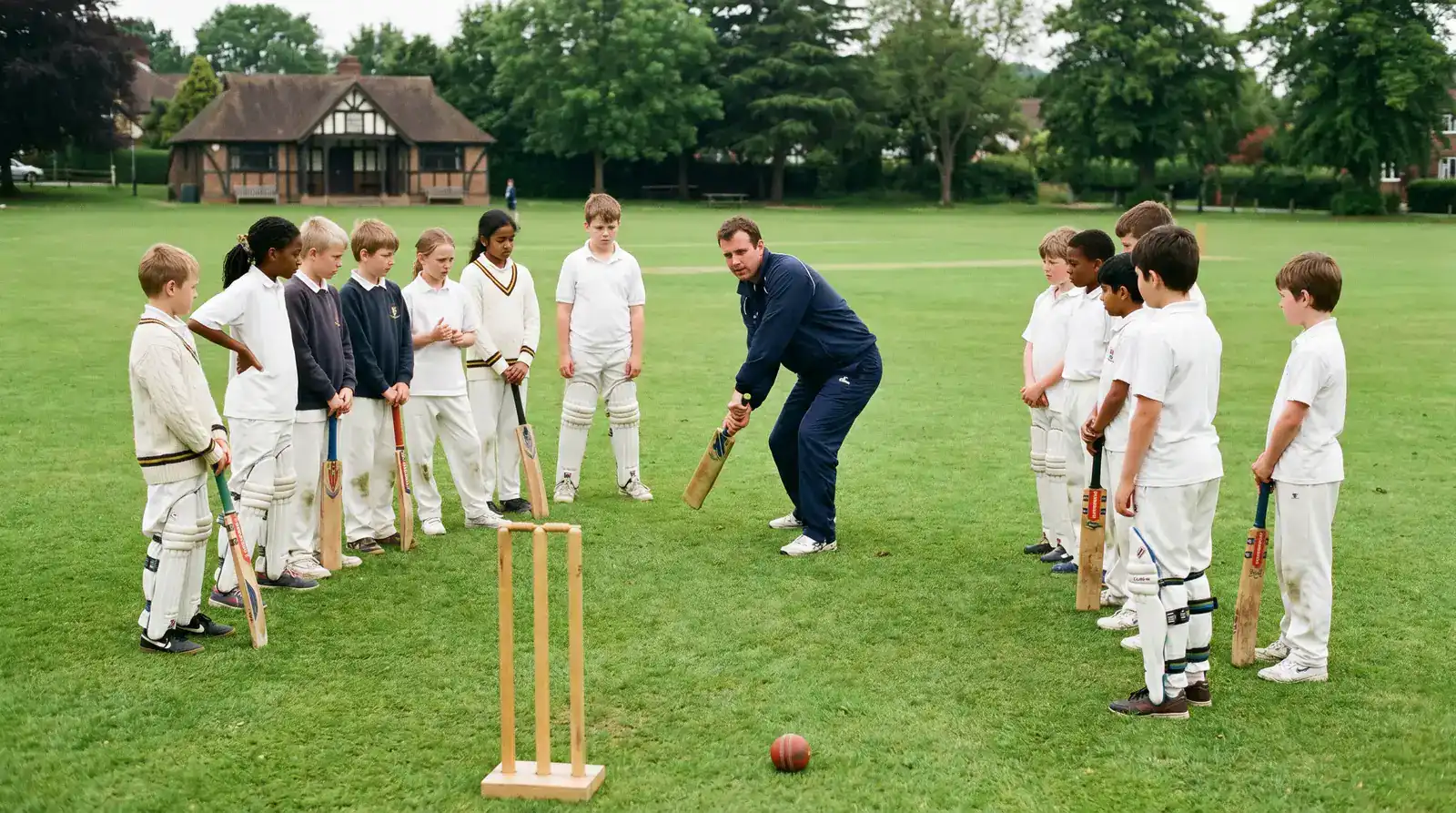 Children in cricket whites holding bats during a grassroots cricket club training session on a UK village green