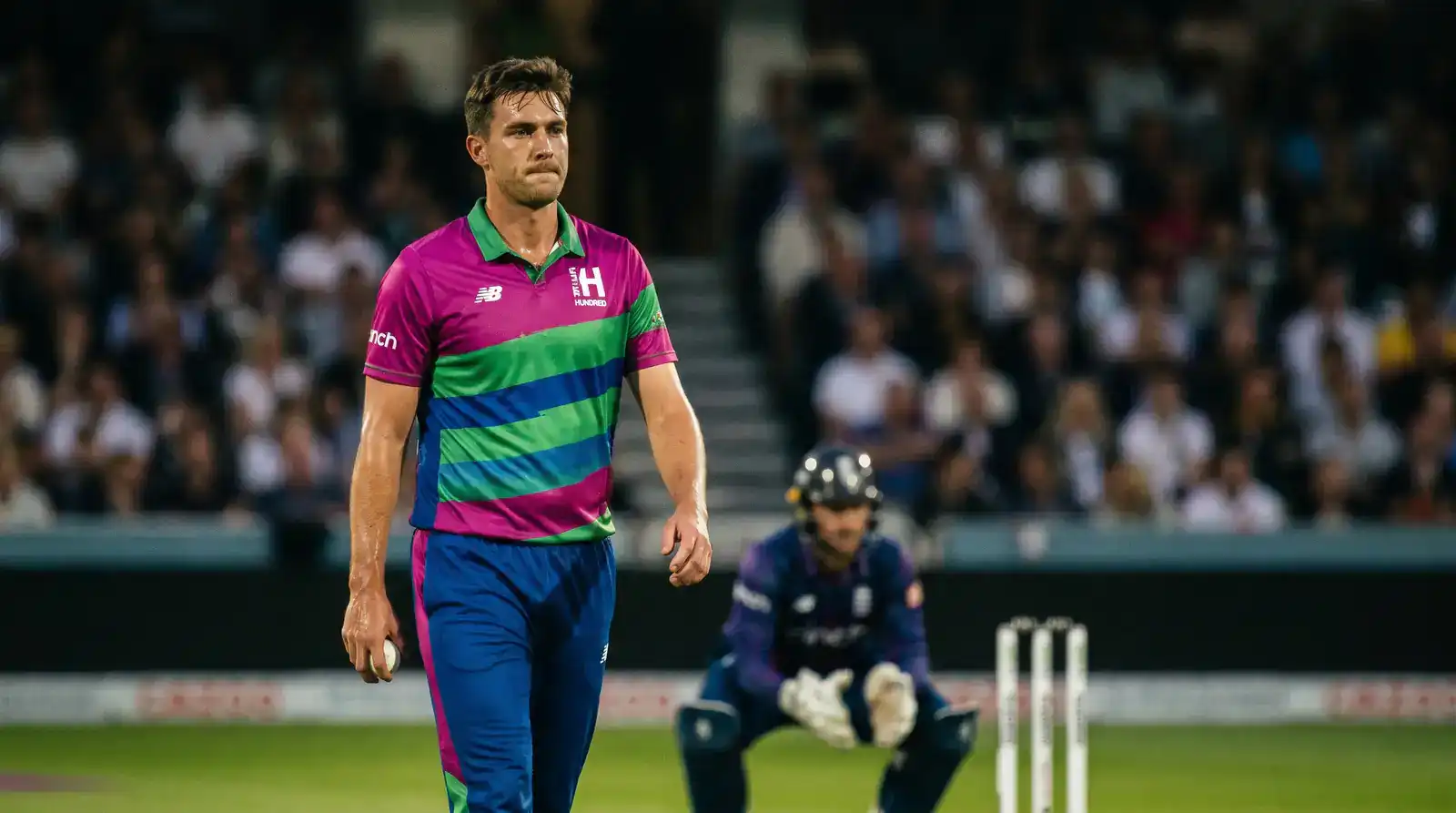 Cricket bowler walking back between five-ball sets at a Hundred match with the wicket-keeper standing up to the stumps