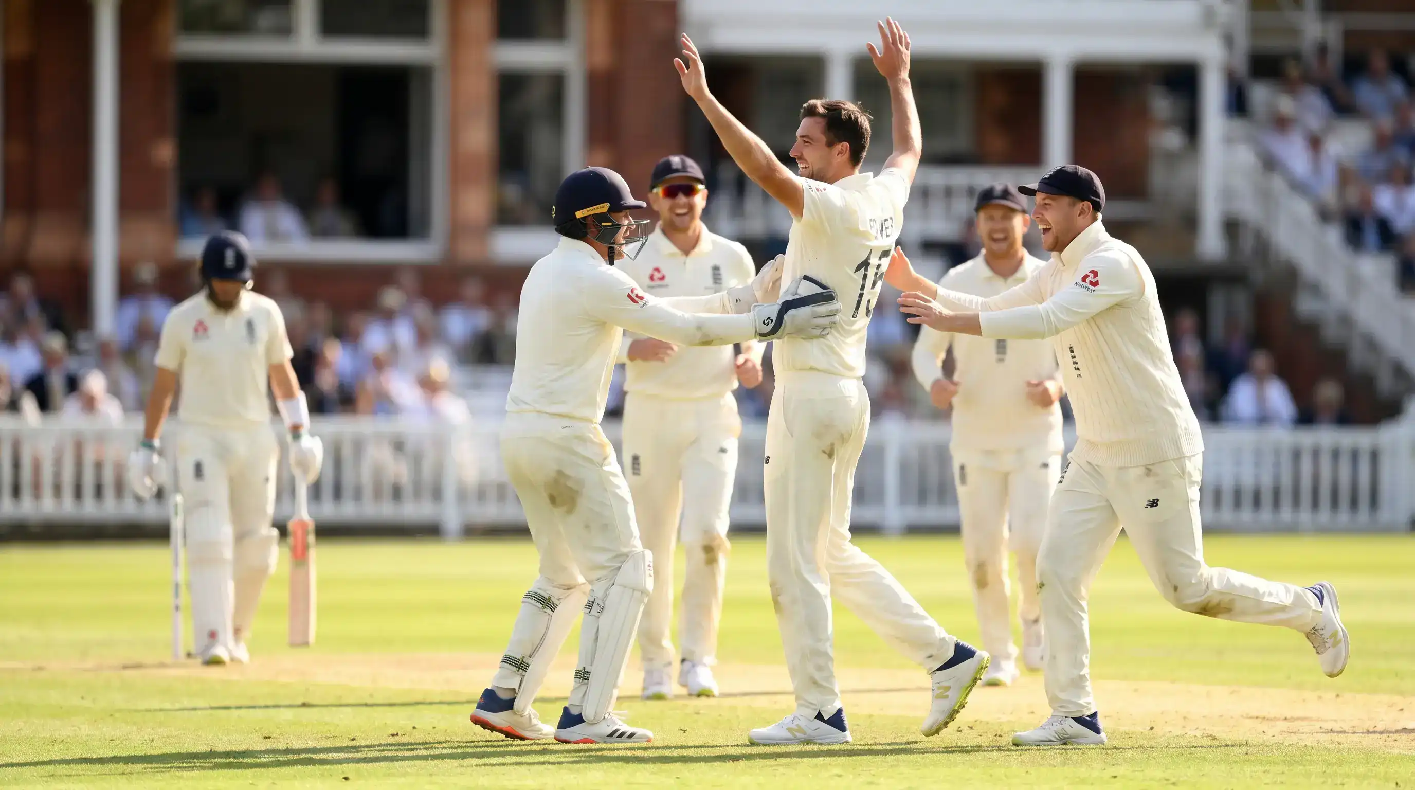 Cricket bowler and team celebrating a wicket in mid-over with the wicket-keeper and slip fielder running in to congratulate