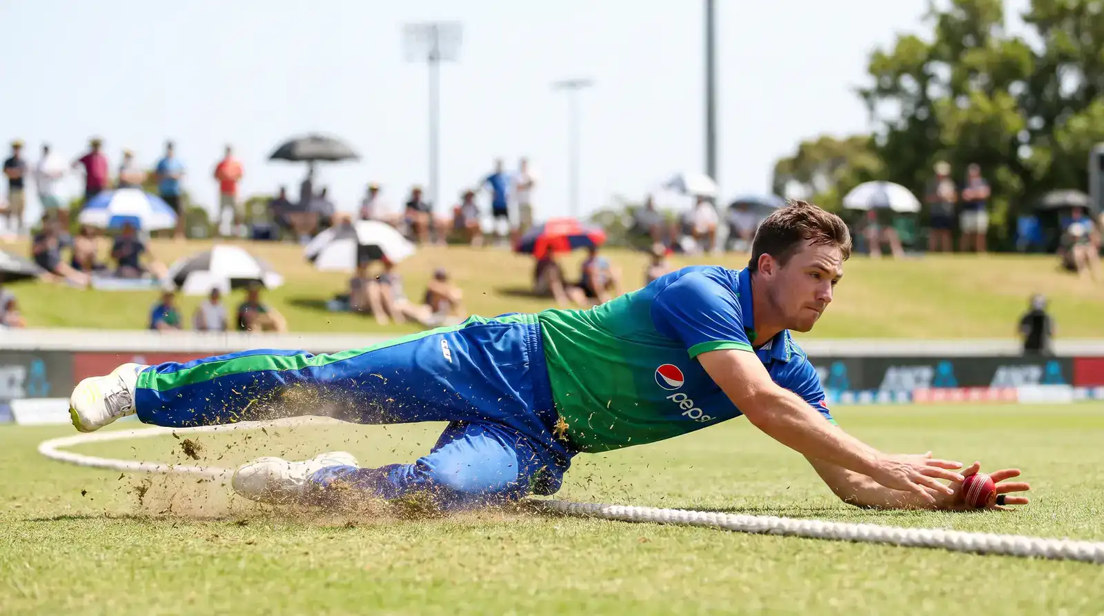 Cricket fielder sliding along the boundary rope to save a four during a county fixture at an English ground
